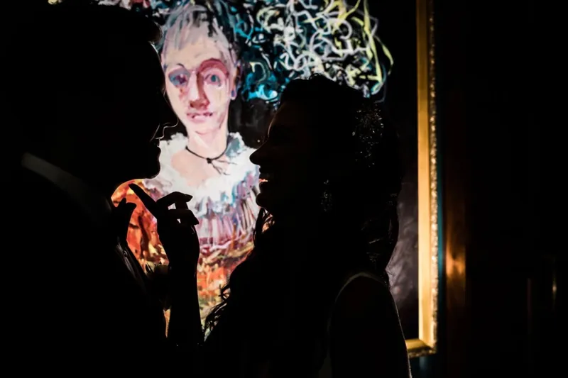 Couple silhouetted in front of a bright painted portrait